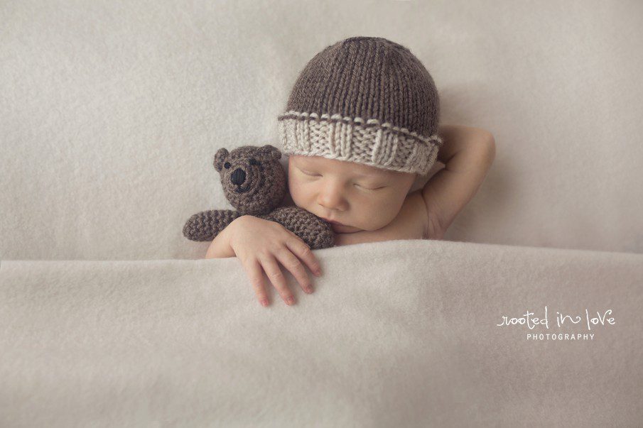 Sleeping newborn baby holding teddy bear.