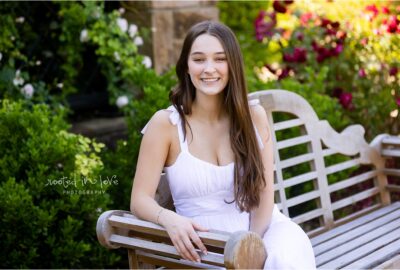 Smiling woman in white dress on bench.